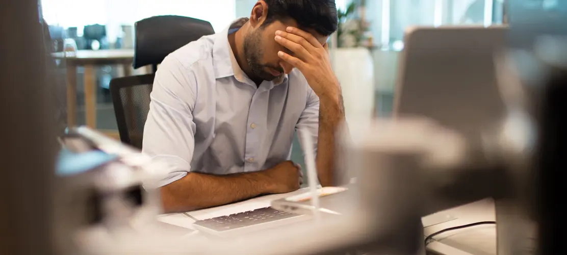 A man sitting in front of a computer covers his eyes with his hand