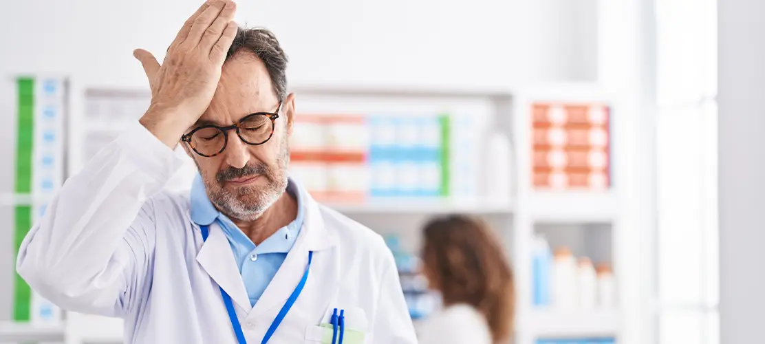 A doctor standing with his eyes closed and his hand pressed to his forehead