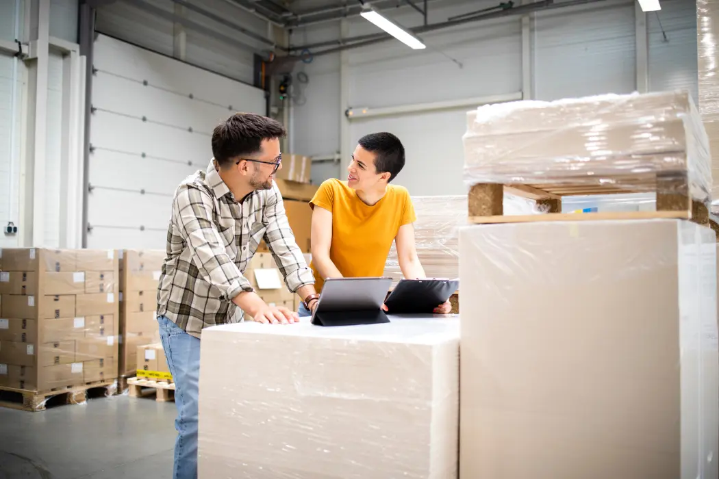 Two people are talking at computers in a warehouse